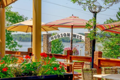 A scenic view of Hudson, Wisconsin, featuring colorful umbrellas, flowers, and a lake in the background.