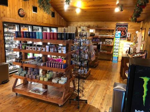 Interior of a rustic store with wooden walls, displaying shelves of drinks, snacks, and souvenirs.