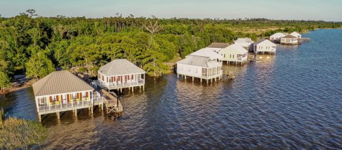 Aerial view of waterfront houses on stilts surrounded by lush greenery and calm water.