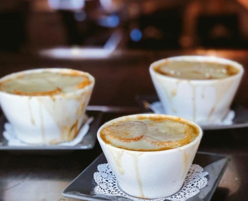 Three bowls of French onion soup with melted cheese, sitting on small plates with lace doilies, slightly overflowing.