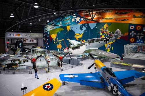 A museum display featuring vintage aircraft, including a P-51 Mustang, against a colorful world map backdrop.