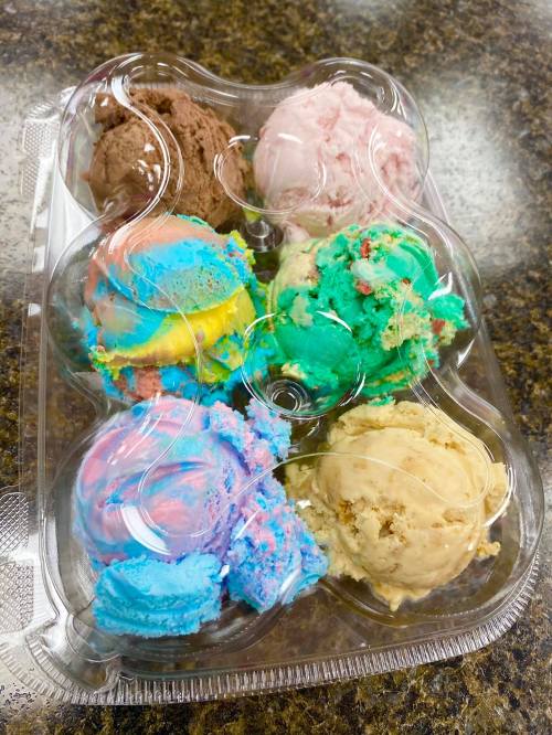A clear container holding six colorful scoops of ice cream in various flavors, including blue, green, pink, and brown.