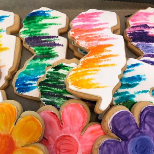 Colorfully decorated cookies shaped like the state of New Jersey, featuring vibrant icing and floral designs.