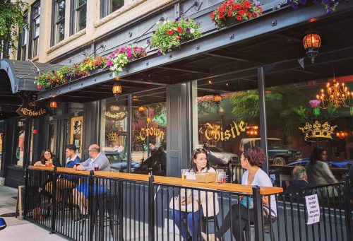 Outdoor seating at a restaurant with flowers, people dining, and a charming urban atmosphere.