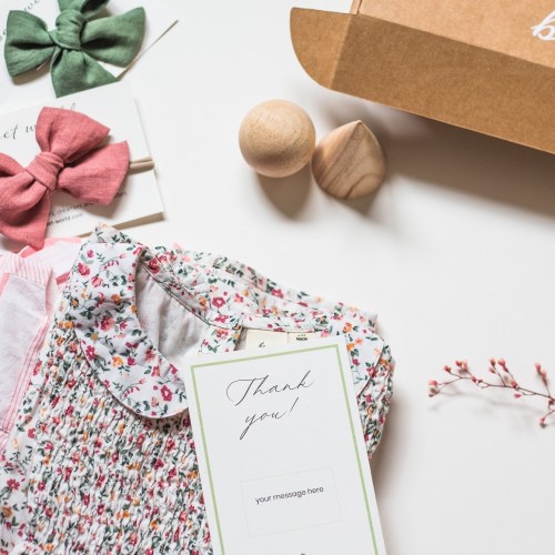 A flat lay of colorful hair bows, a floral dress collar, wooden toys, and a thank you card on a light background.