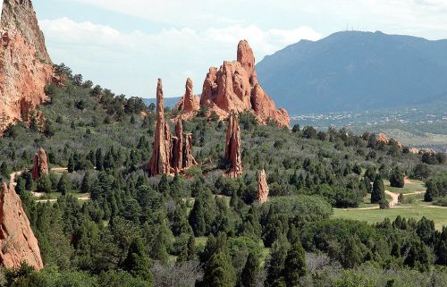 A scenic view of red rock formations surrounded by lush greenery and distant mountains under a blue sky.