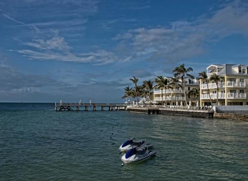 A serene waterfront scene featuring jet skis, a pier, and a palm-lined resort under a blue sky.