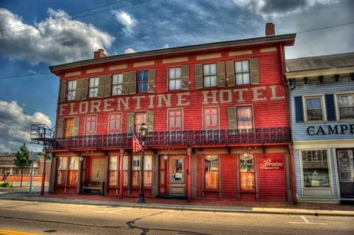 Historic red building with "Florentine Hotel" sign, featuring balconies and an American flag, under a cloudy sky.