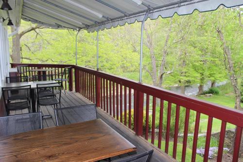 A wooden deck with tables and chairs overlooks a lush green landscape and a flowing stream.