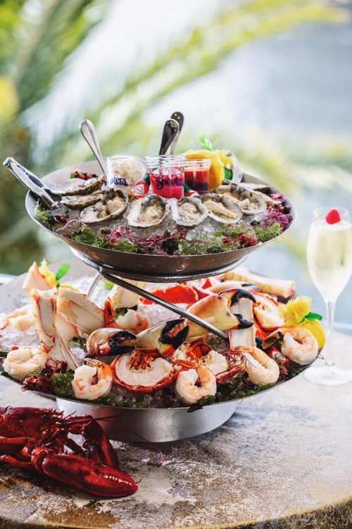 A two-tier seafood platter featuring oysters, shrimp, crab, and lobster, garnished with lemon and sauces.