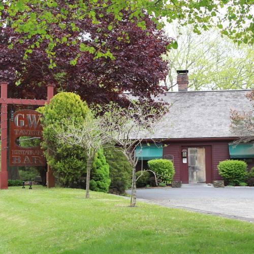 A rustic tavern with a sign, surrounded by green trees and shrubs, on a sunny day.