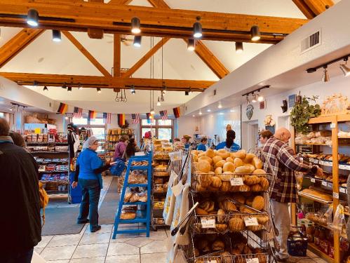 A bustling bakery with wooden beams, shelves of bread, and customers browsing various baked goods.