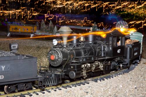 A model steam train with a glowing light effect, surrounded by festive decorations and miniature trees.