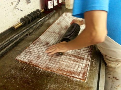 A person rolls out dough on a floured surface, creating a grid pattern with a rolling pin.