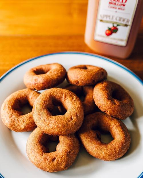 A plate of freshly baked donuts with a bottle of apple cider in the background.