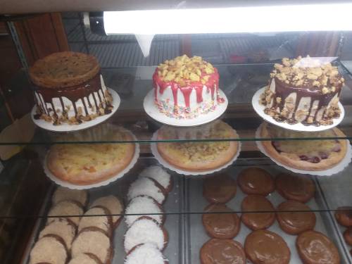 A display case filled with various cakes and pies, including chocolate-drizzled cakes and fruit-topped desserts.