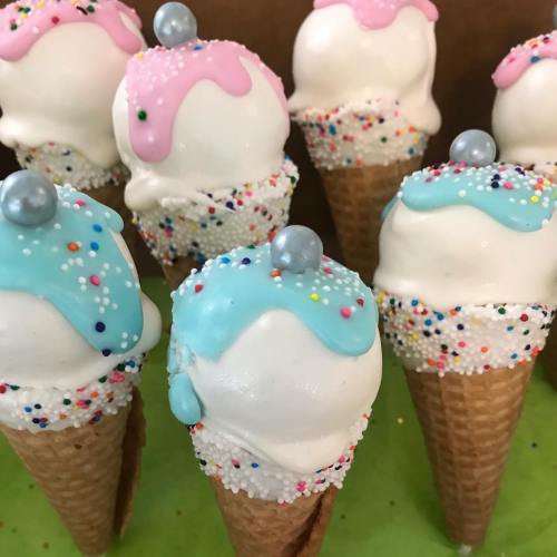 Colorful ice cream cones with white scoops, pink and blue drizzles, and sprinkles, topped with shiny pearls.