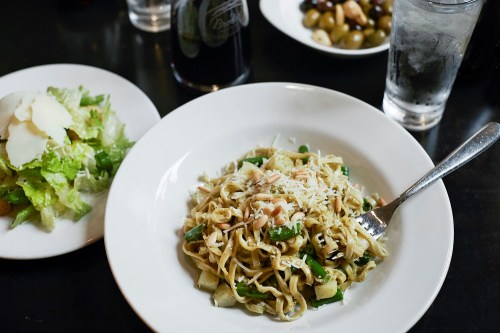 A plate of pasta with vegetables and cheese, accompanied by a side salad and a glass of water.