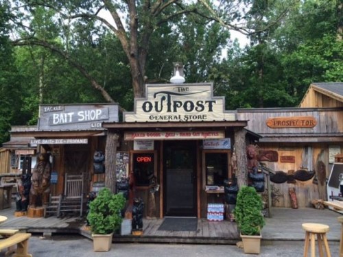 A rustic general store with wooden signage, featuring a bait shop and prospector theme, surrounded by trees.