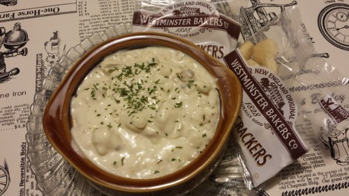 A bowl of creamy soup garnished with herbs, accompanied by Westminster Bakers crackers on a patterned tablecloth.