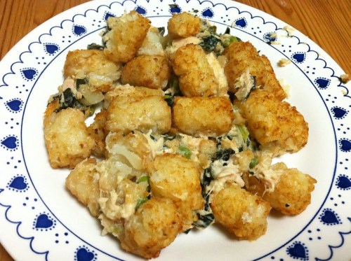 A plate of crispy tater tots mixed with creamy spinach and chicken, garnished with herbs.