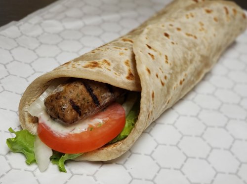 A grilled meat wrap with lettuce, tomato, and sauce, wrapped in a soft flatbread on a patterned paper.