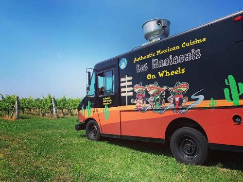 A colorful food truck featuring Mexican cuisine, parked near a vineyard under a clear blue sky.