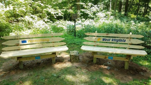 Two wooden benches labeled "Pennsylvania" and "West Virginia" in a lush green park setting.