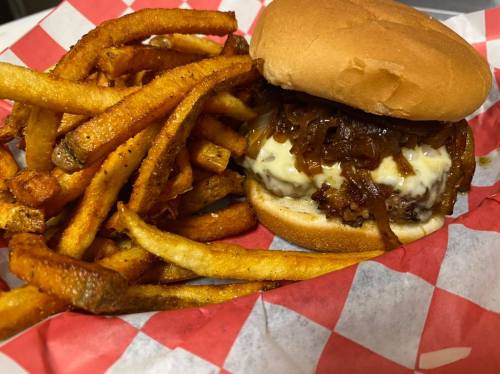 A juicy burger with melted cheese and caramelized onions, served with a side of crispy fries in a red-checkered basket.