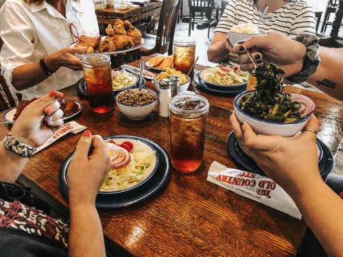A group of people enjoying a meal at a restaurant, featuring plates of food and drinks on a wooden table.