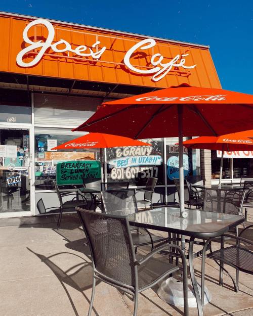 Exterior of Joe's Café with orange awning, outdoor seating, and Coca-Cola umbrellas on a sunny day.