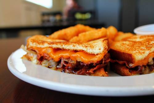 A close-up of a grilled cheese sandwich with melted cheese and onions, served with crispy fries on a white plate.