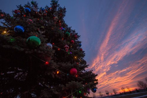 A decorated Christmas tree with colorful ornaments and lights against a vibrant sunset sky.