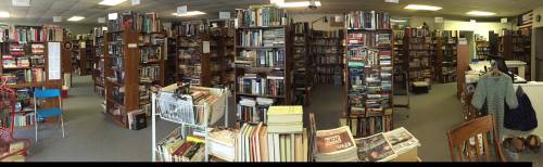 A panoramic view of a cozy bookstore filled with tall shelves of books and a few chairs scattered throughout.