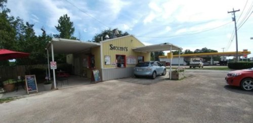 A small, yellow building with a covered patio, featuring a sign for "Saxon's" and parked cars in the lot.