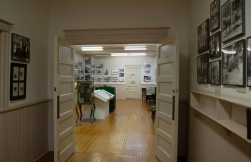Interior of a museum hallway with open doors, showcasing black-and-white photographs on the walls and display cases.