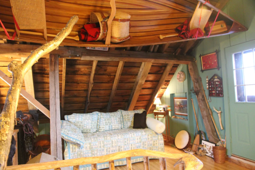 Cozy attic interior with a blue couch, wooden beams, and rustic decor, featuring hanging canoes and a green door.