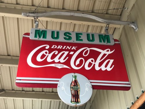 Sign for a museum featuring a vintage Coca-Cola advertisement, with bold red and green colors.
