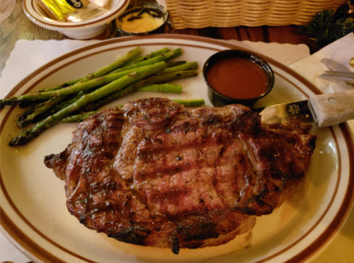 A grilled steak served with asparagus and a small bowl of sauce on a plate.
