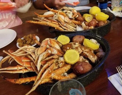 Two trays of seafood featuring crabs, potatoes, and lemon slices, served on a wooden table.