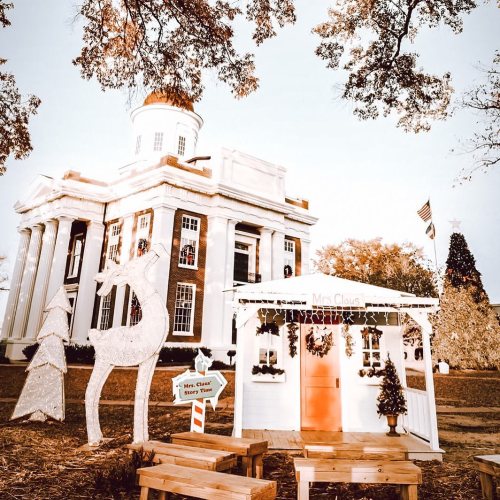 A festive scene featuring a decorated building, a reindeer, and a small holiday cabin labeled "Mrs. Claus."