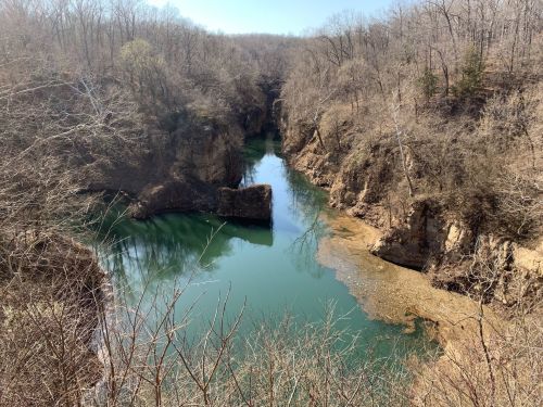 A serene river winding through a rocky landscape, surrounded by bare trees and a clear blue sky.