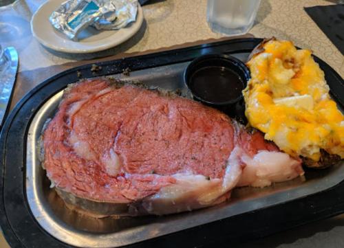 A plate with a large slice of prime rib and a loaded baked potato topped with cheese and butter.