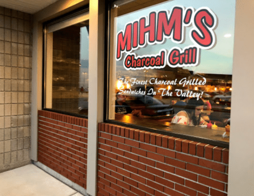 A restaurant window displaying "MIHM'S Charcoal Grill" sign and a view of diners inside.