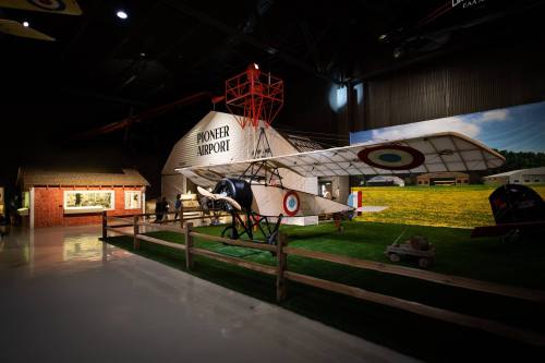A vintage airplane displayed in a museum, with a model airport building and grassy area in the background.