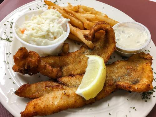 A plate of fried fish fillets with a lemon wedge, coleslaw, and French fries, served with a dipping sauce.