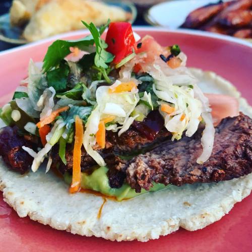 A close-up of a taco topped with grilled meat, fresh vegetables, and salsa on a pink plate.