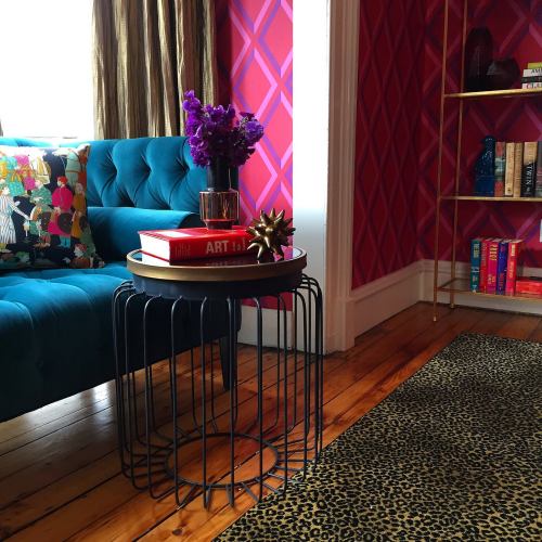 A cozy living room corner featuring a blue sofa, a round black side table with books, and a vase of purple flowers.