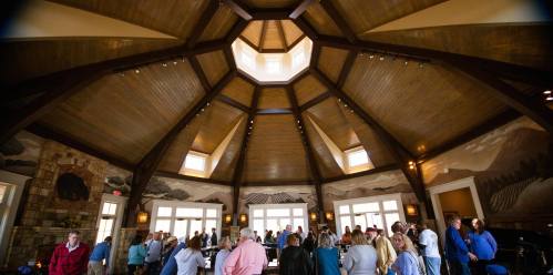 A spacious, circular room with a high wooden ceiling and large windows, filled with people socializing.