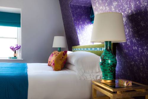 A stylish bedroom featuring a bed with colorful pillows, a vibrant purple wall, and a decorative lamp on a side table.